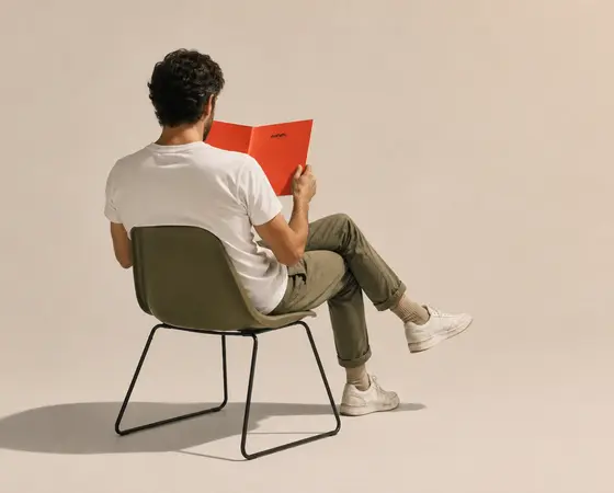 A person sitting in a low chair, reading a red booklet.
